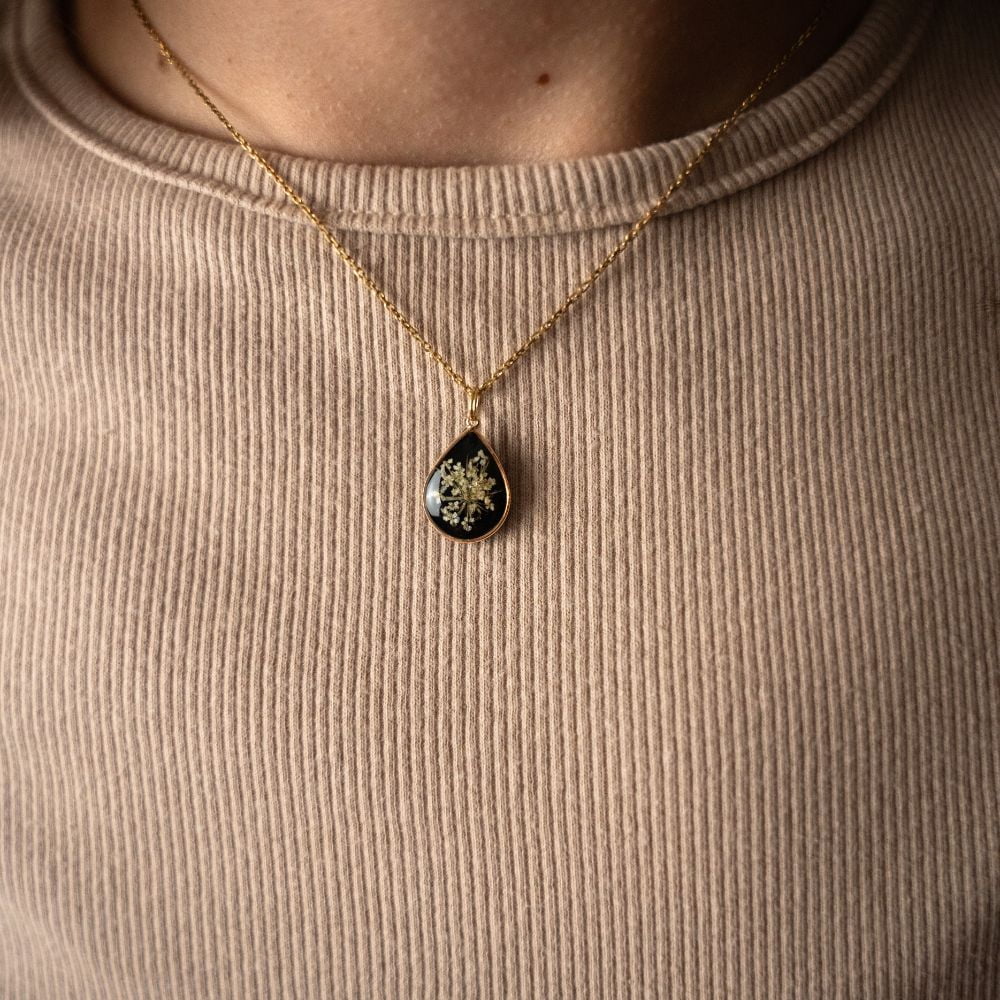 Teardrop gold plated necklace with real lace flowers preserved in resin on black background.