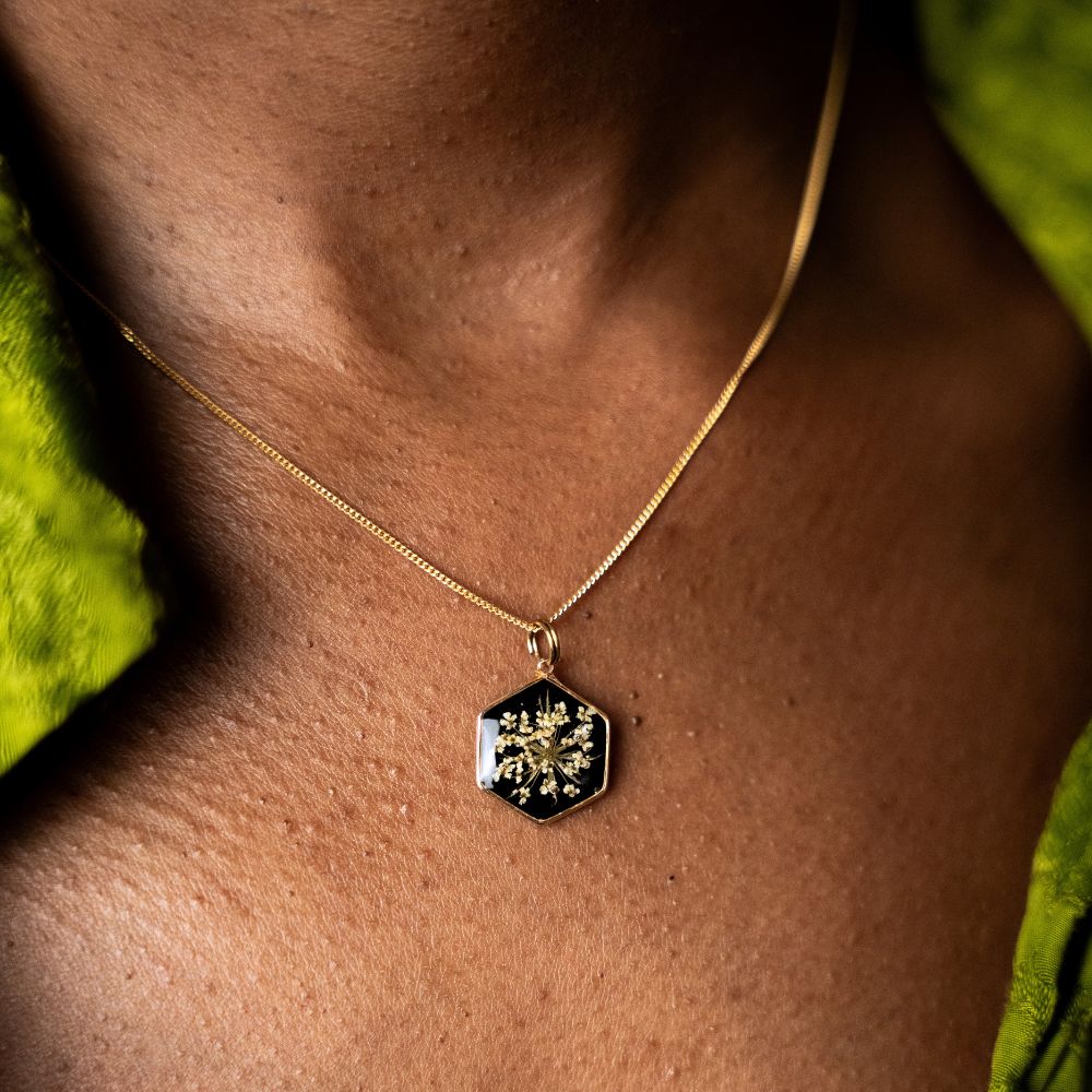 Hexagon gold plated necklace with real wild lace flowers preserved in resin on black background.