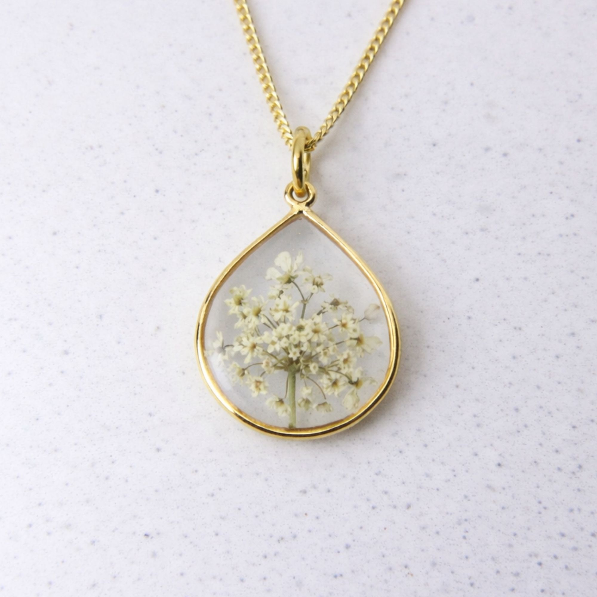 Gold teardrop pendant with preserved wild lace flowers set in clear resin on a gold chain.