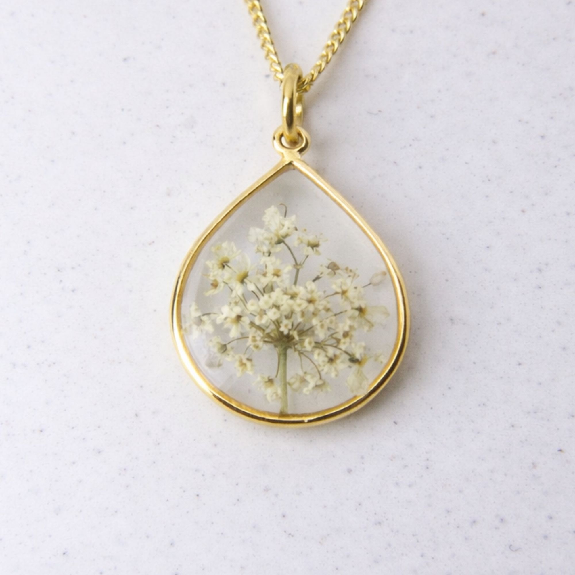 Gold teardrop pendant with preserved wild lace flowers set in clear resin on a gold chain.
