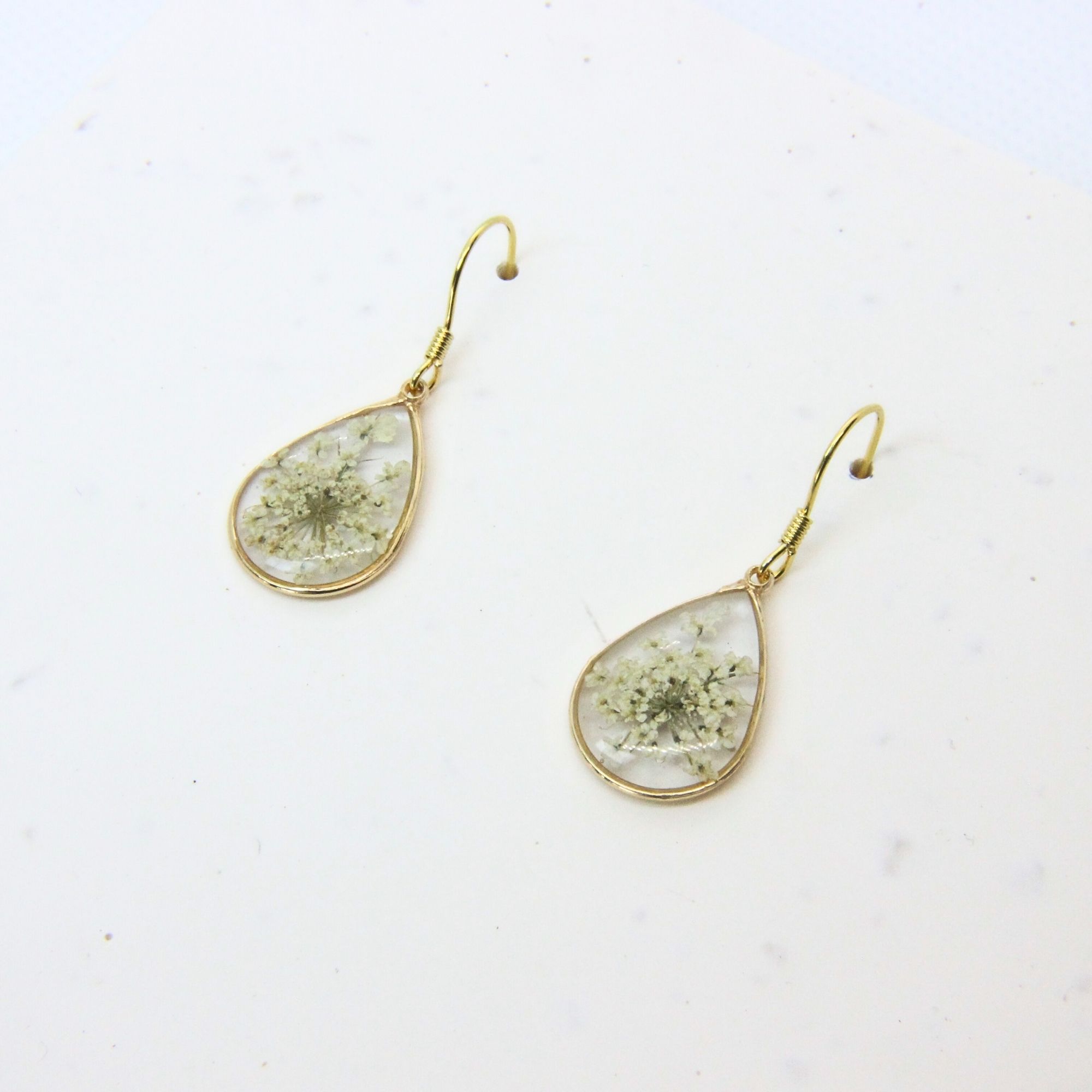 Gold plated teardrop resin earrings with white lace flowers preserved in clear resin and gold plated sterling silver hooks.