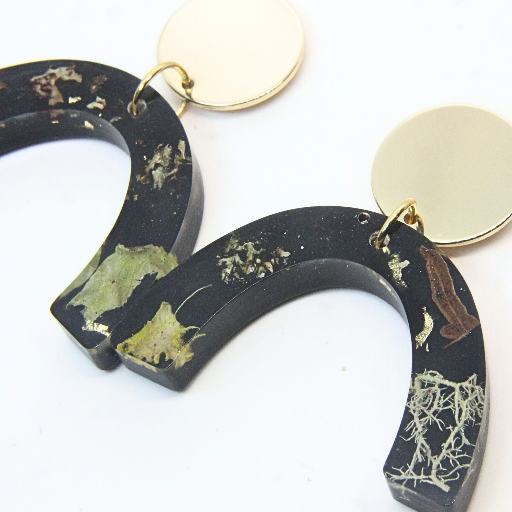 Black resin curved arch earrings with wild lichen, fern and moss inlay, gold plated brass disc tops and sterling silver studs.