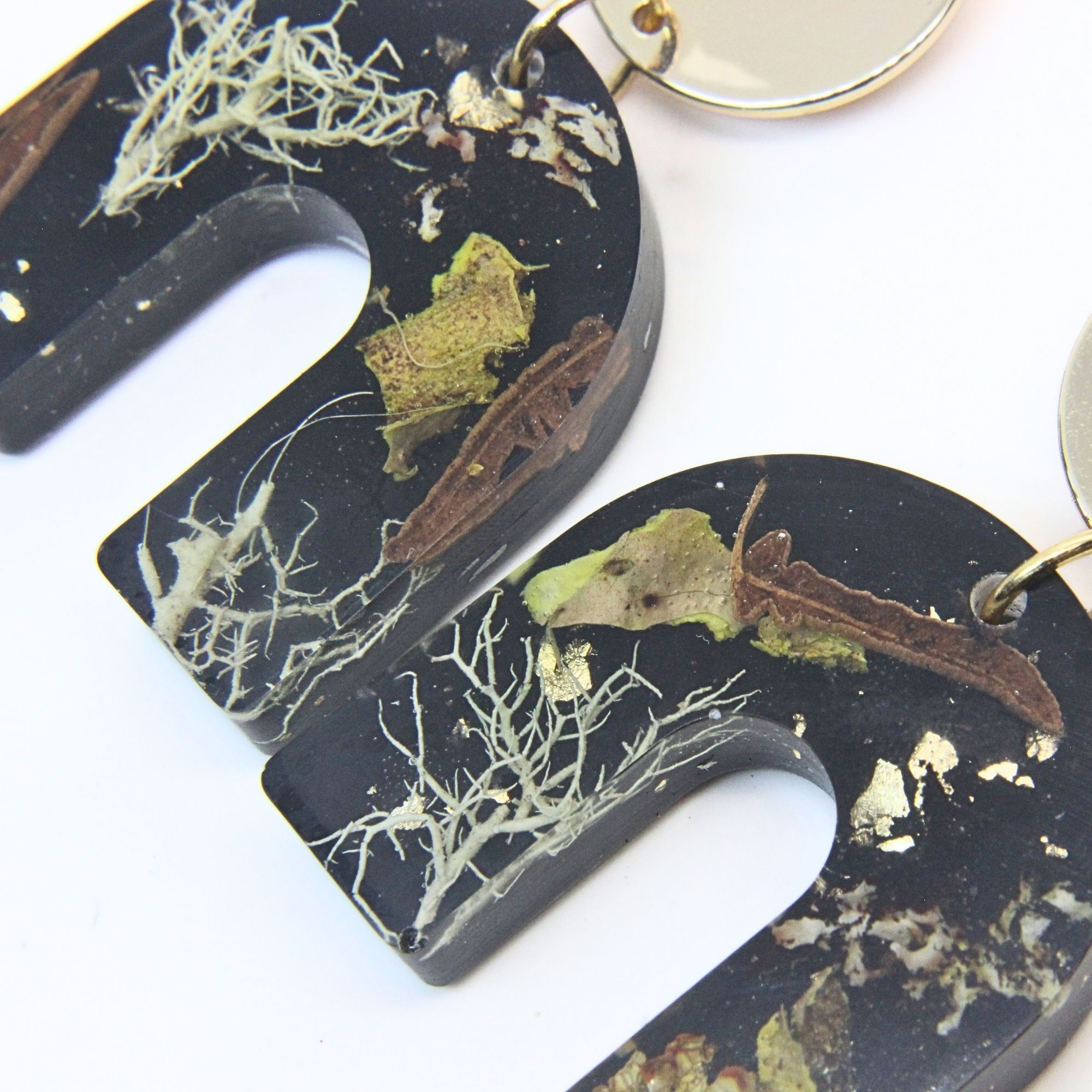 Black solid resin arch earrings with grass seed inlay and gold plated sterling silver disc tops.