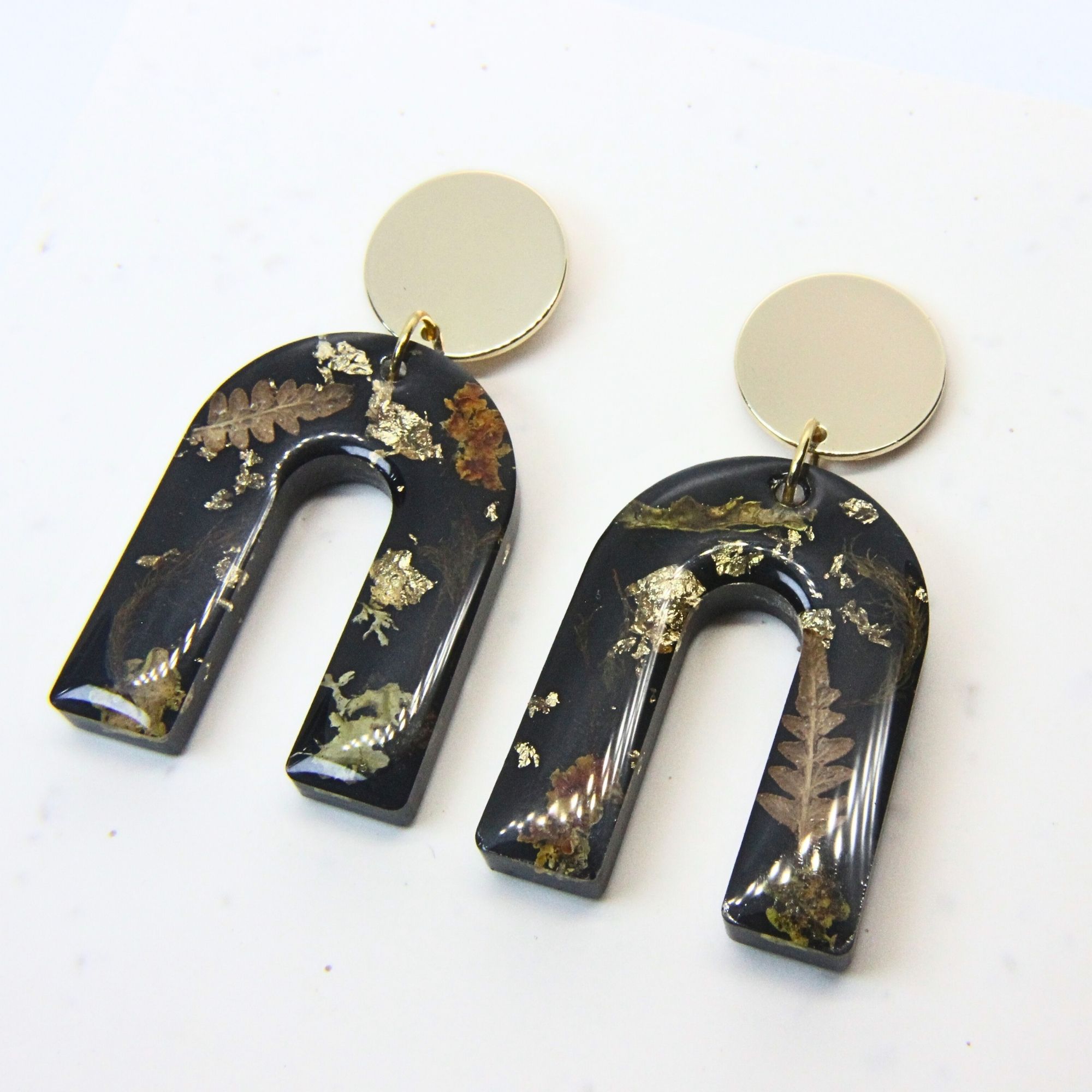Black resin arch earrings with grass seed inlay and gold flecks, finished with gold plated sterling silver disc tops.