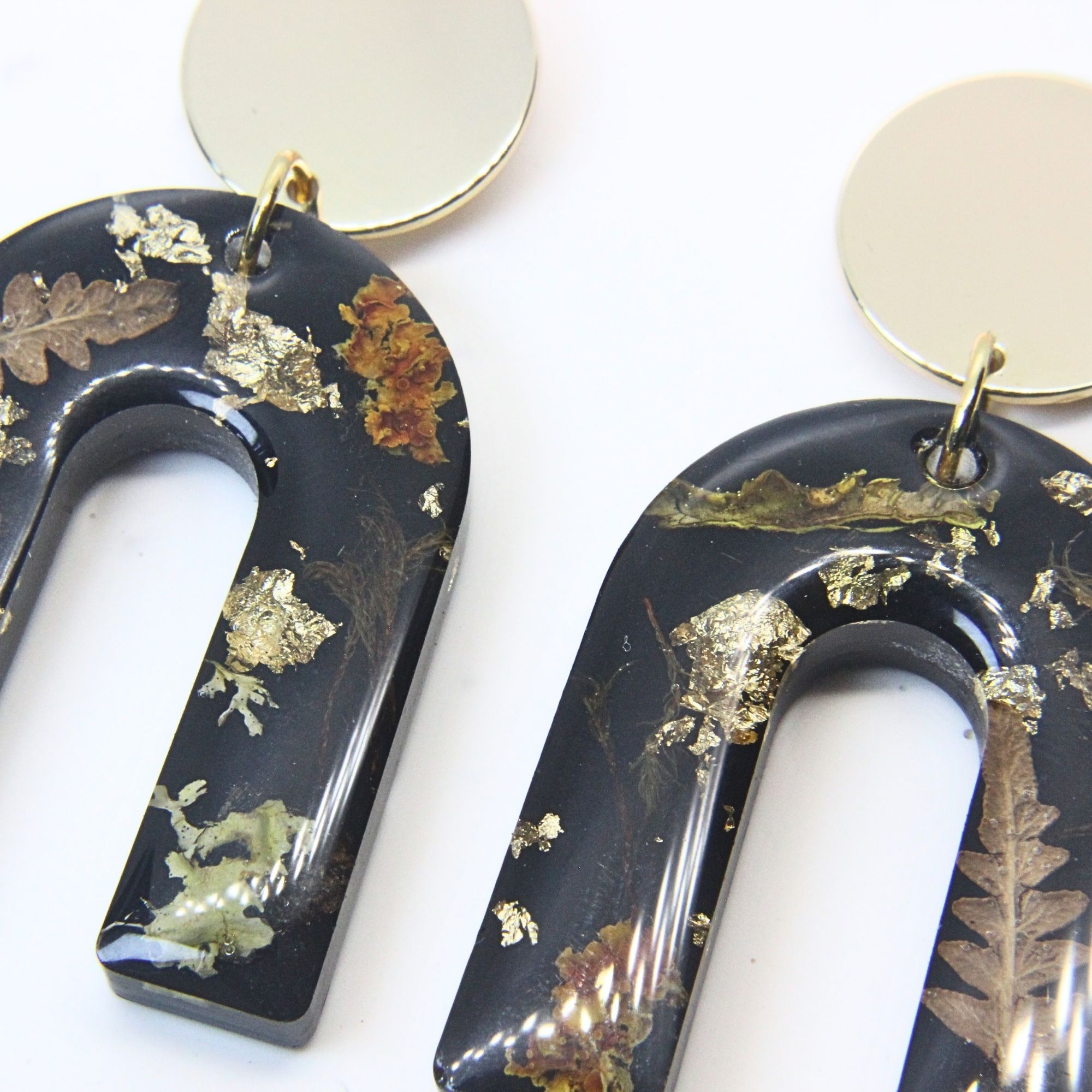Black resin arch earrings with grass seed inlay and gold flecks, finished with gold plated sterling silver disc tops.