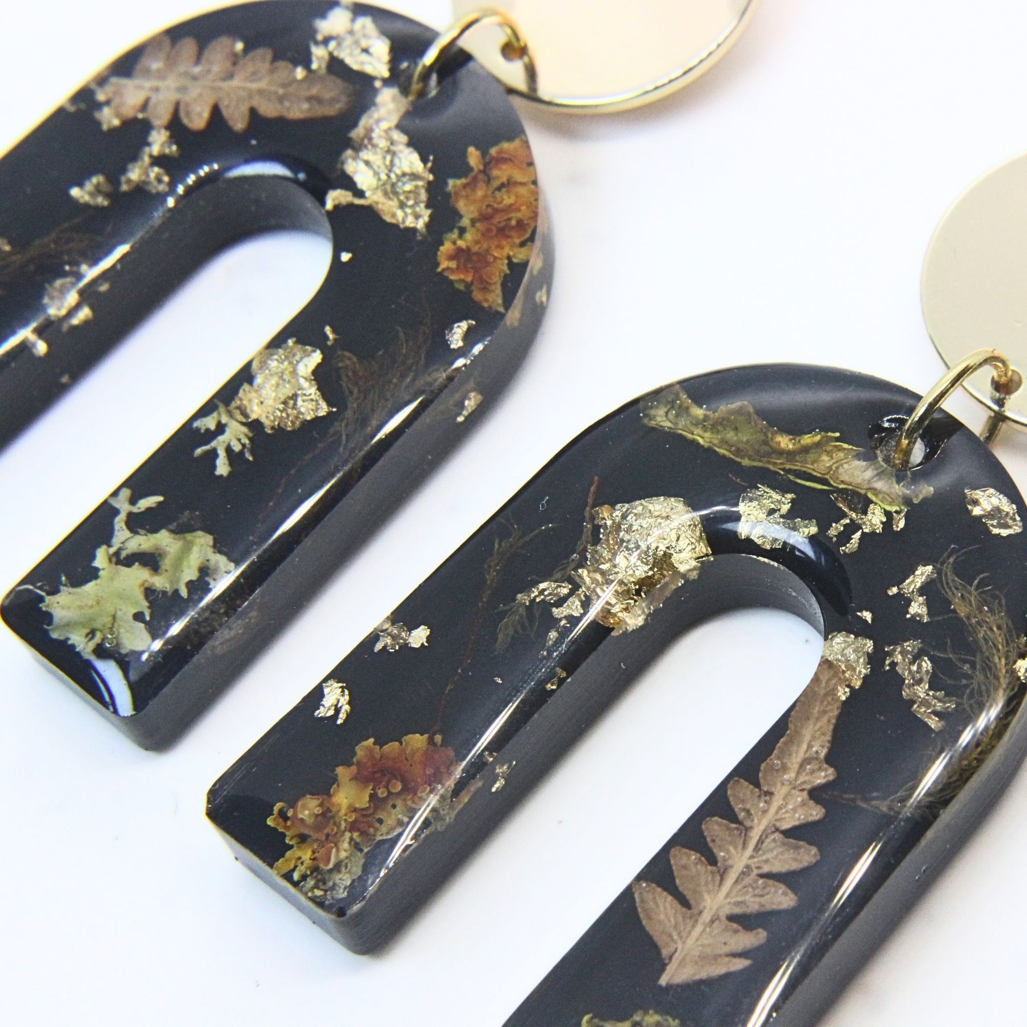 Black resin arch earrings with grass seed inlay and gold flecks, finished with gold plated sterling silver disc tops.