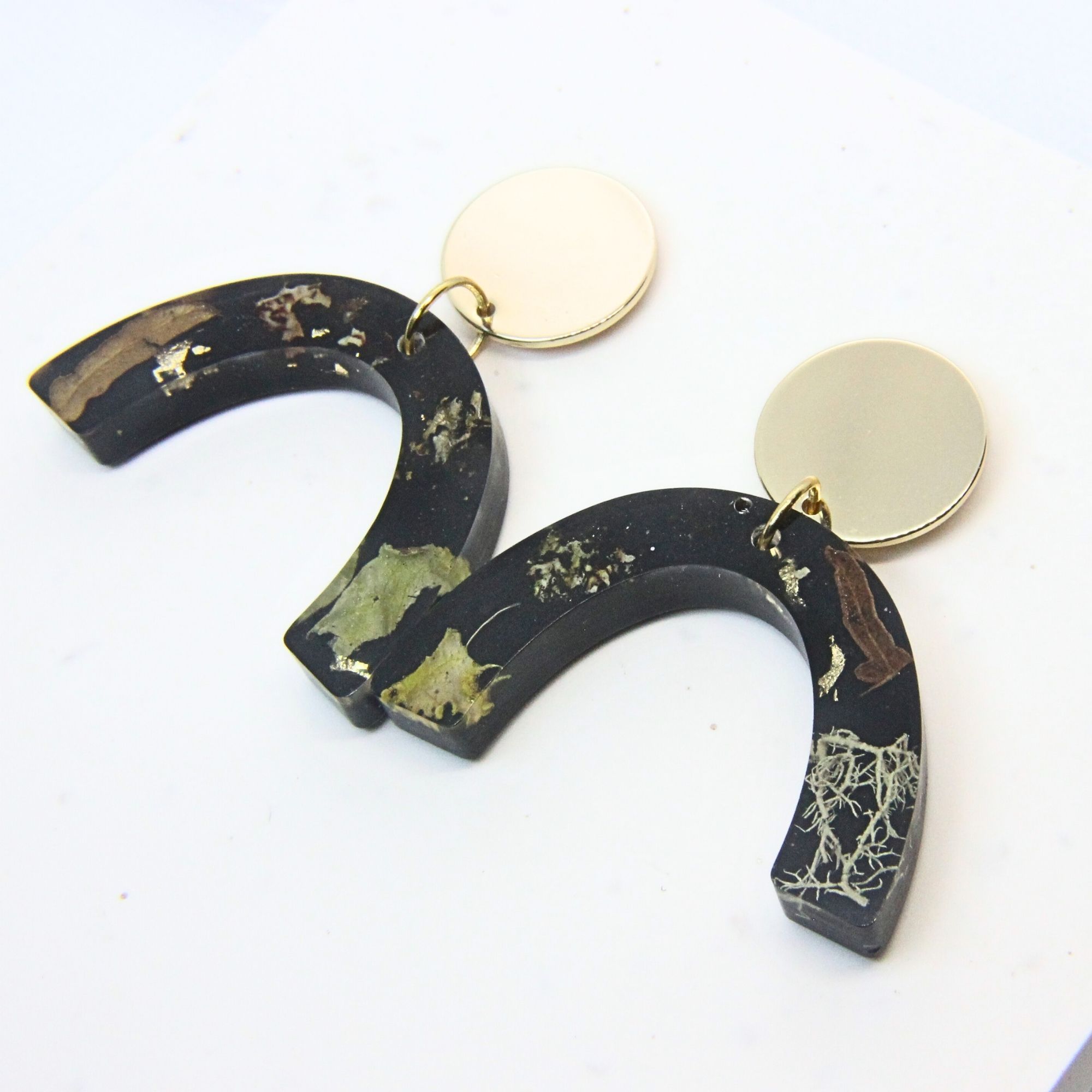 Black resin curved arch earrings with wild lichen, fern and moss inlay, gold plated brass disc tops and sterling silver studs.