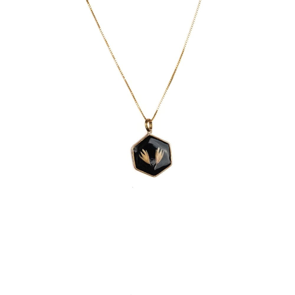 Hexagon gold necklace with real grass seeds preserved in resin on black background.