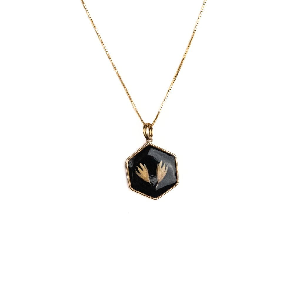 Hexagon gold necklace with real grass seeds preserved in resin on black background.