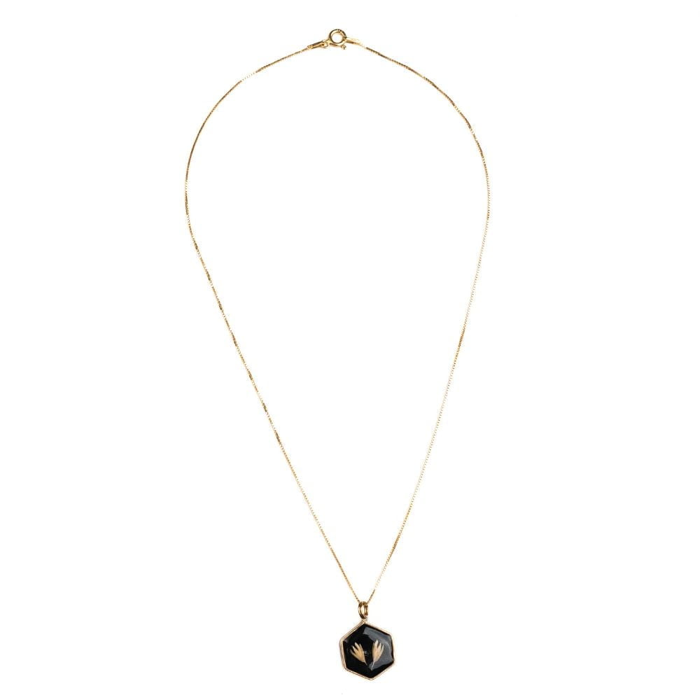 Hexagon gold necklace with real grass seeds preserved in resin on black background.