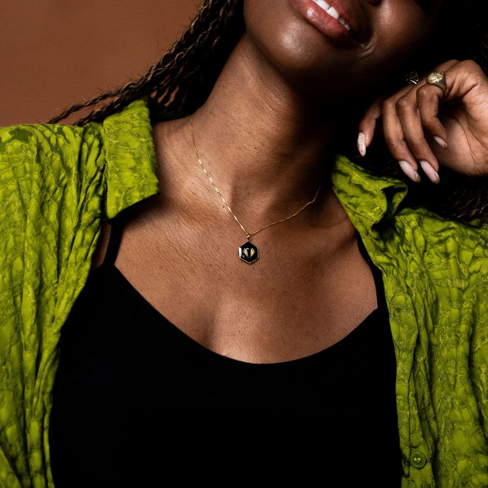 Hexagon gold necklace with real grass seeds preserved in resin on black background.