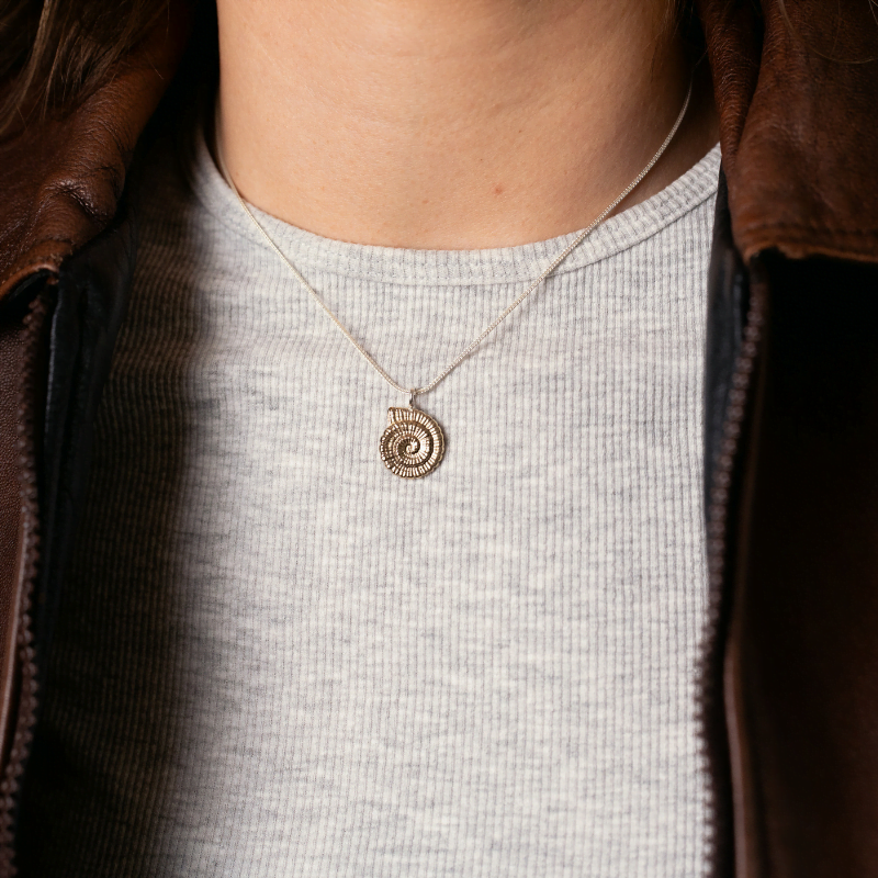 Brass ammonite pendant necklace on sterling silver chain worn layered with gold chain.