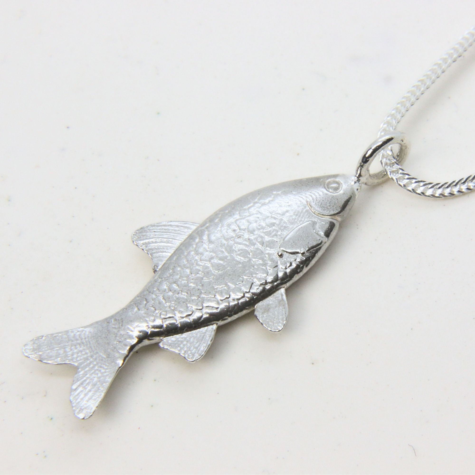 Sterling silver fish pendant necklace with detailed texture.