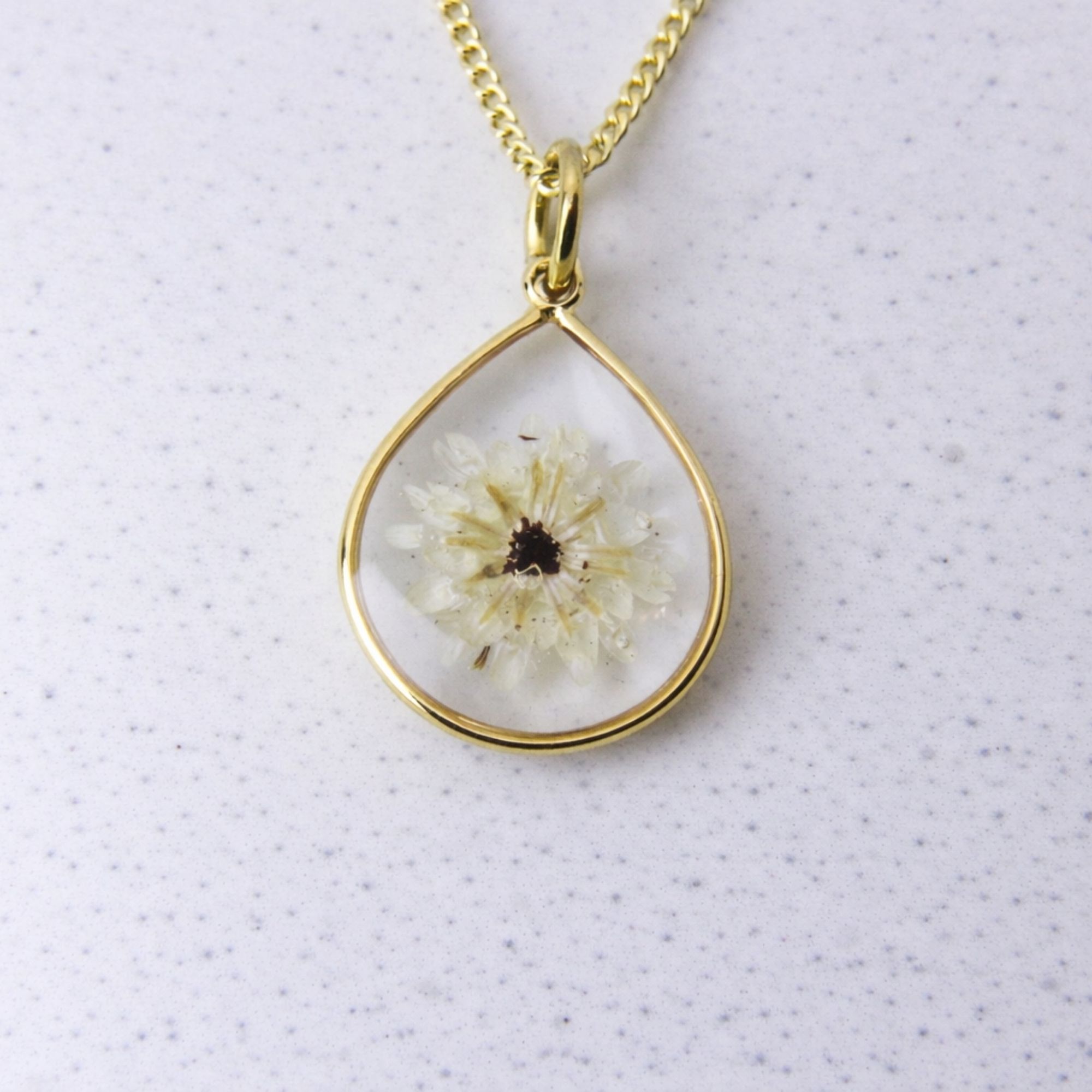 Gold teardrop pendant with a preserved white fynbos flower set in clear resin on a gold chain.