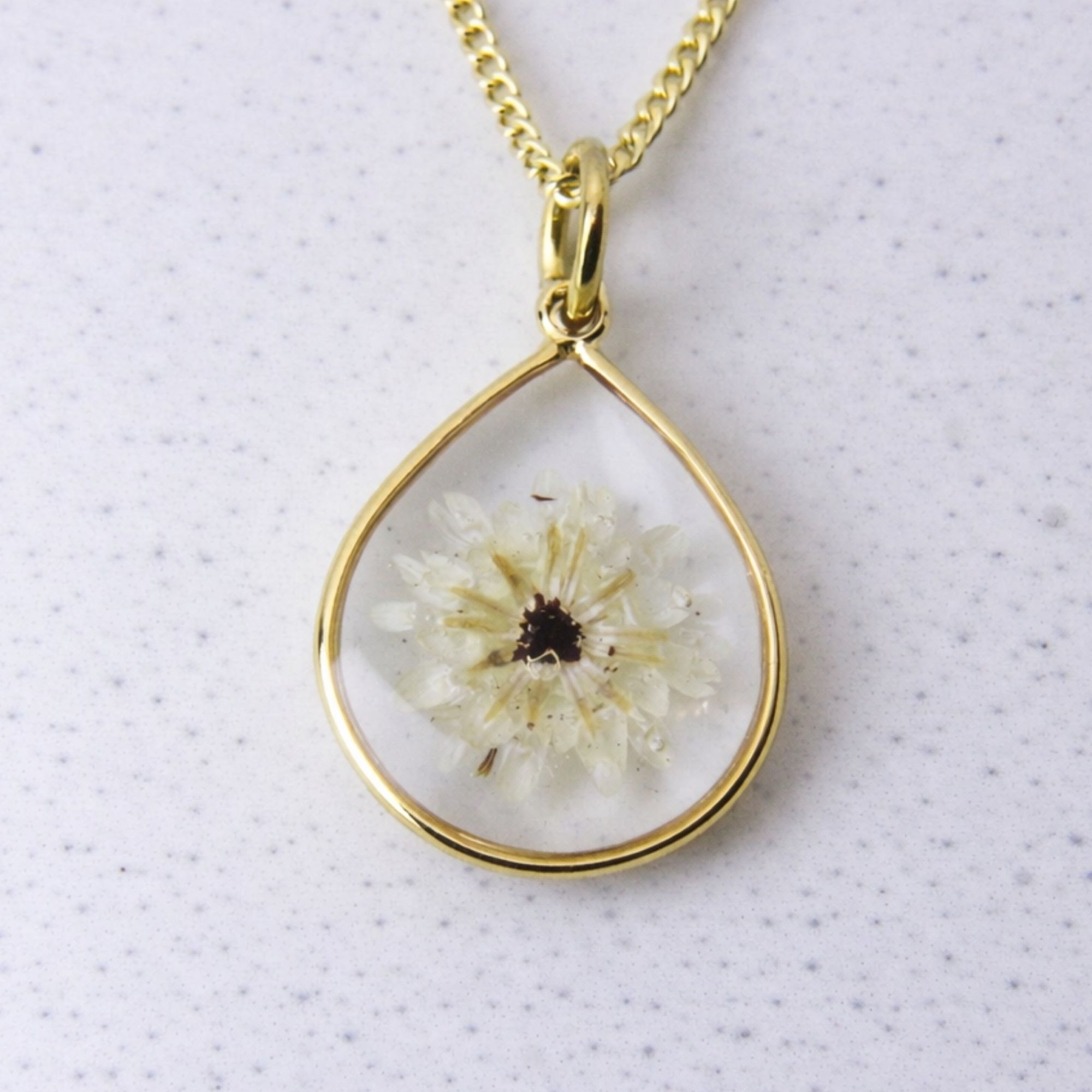 Gold teardrop pendant with a preserved white fynbos flower set in clear resin on a gold chain.