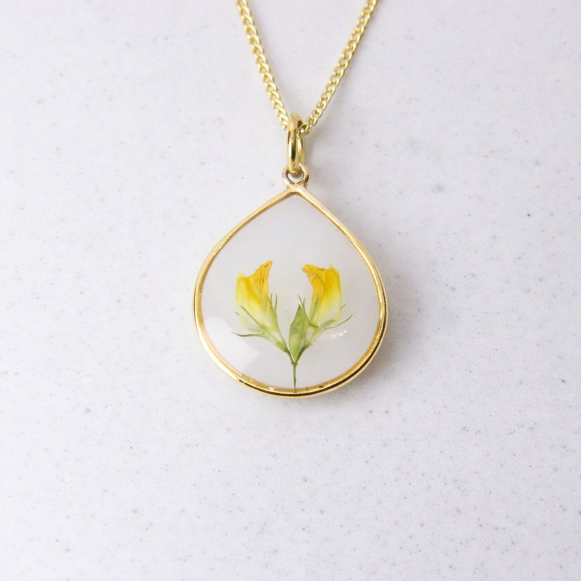 Gold teardrop pendant with preserved yellow flowers set in clear resin on a gold chain.