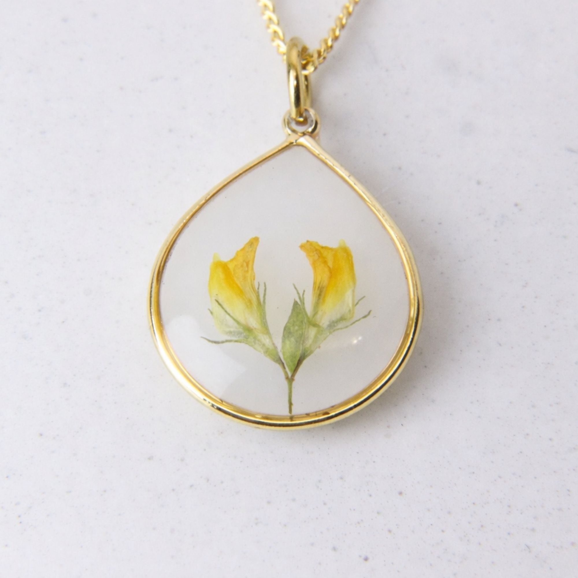 Gold teardrop pendant with preserved yellow flowers set in clear resin on a gold chain.