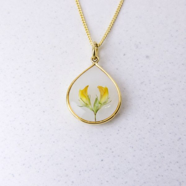 Gold teardrop pendant with preserved yellow flowers set in clear resin on a gold chain.