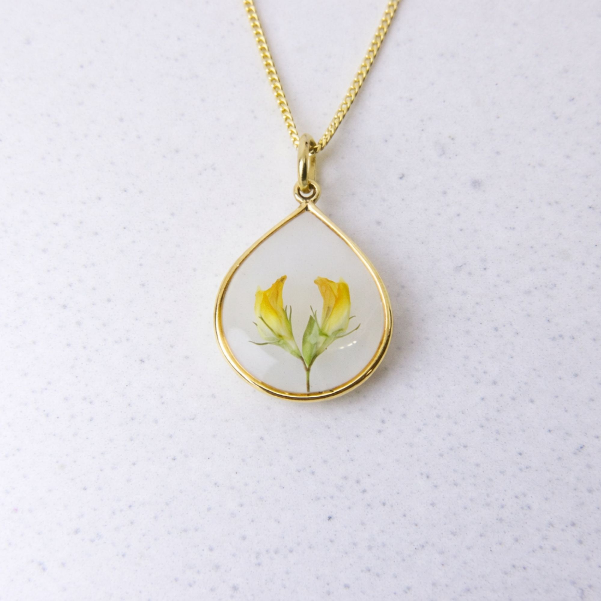 Gold teardrop pendant with preserved yellow flowers set in clear resin on a gold chain.