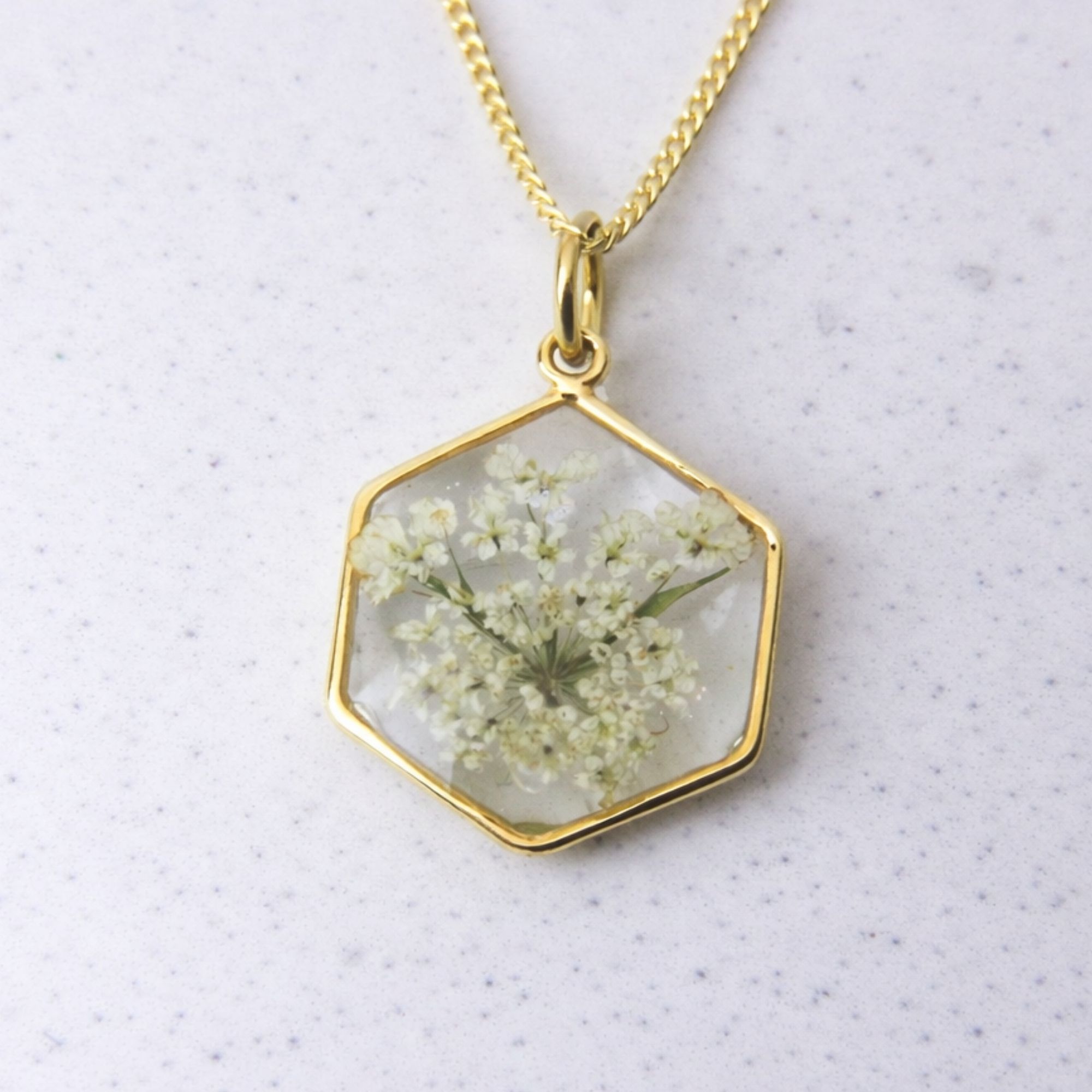 Gold hexagon pendant with preserved wild lace flower set in clear resin on a gold chain.