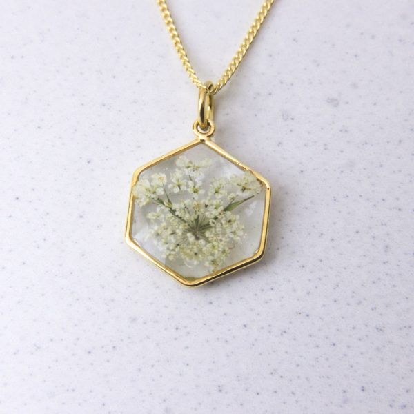 Gold hexagon pendant with preserved wild lace flower set in clear resin on a gold chain.